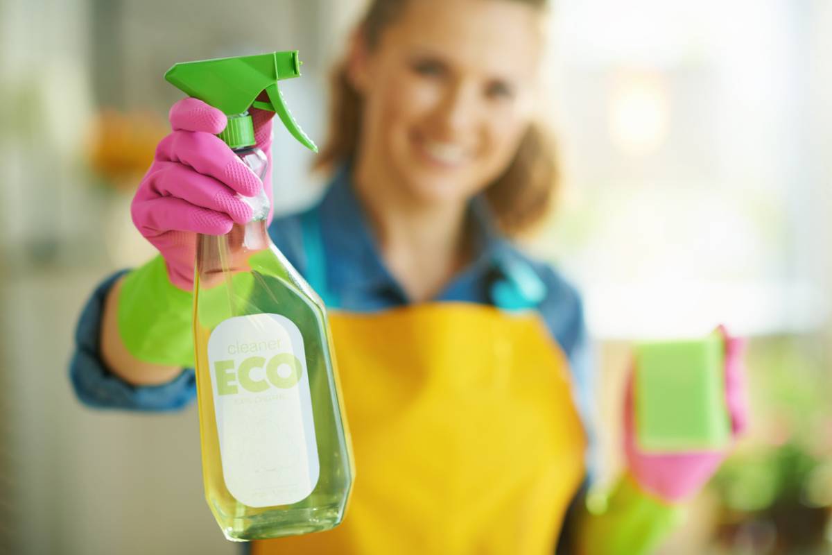 Agente d’entretien en gants roses tendant un spray nettoyant écologique